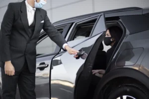 Chauffeur in Mask Assisting Passenger into Luxury Car