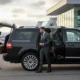 Professional chauffeur assisting passenger with luggage beside luxury black SUV by Noor Limousine LLC at New Jersey airport