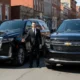 Professional chauffeur standing between two black luxury SUVs parked on a city street, representing Ocean County limo service.